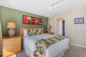 Ein Schlafzimmer mit Bett, Nachttischen, Deckenventilator und Kunstwerken an den Wänden.