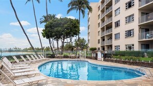 A swimming pool with lounge chairs, a stone deck, and a building with balconies. - Oceanfront Bliss at Royal Mauian #405–Stunning Views, Prime South Kihei Location (Kihei, Maui)
