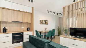 A modern kitchen with white cabinets, a built-in oven, and a dining area with a table and chairs. - Stylish Studio in Jeżyce | Private Parking and Balcony (Poznan)