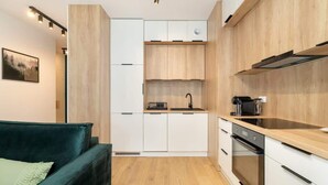 A modern kitchen with wooden cabinets, a built-in oven, and a countertop microwave. - Stylish Studio in Jeżyce | Private Parking and Balcony (Poznan)