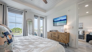 A bedroom with a large bed, a wooden dresser, a TV, and a view of the outdoors.