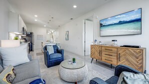 A modern living room with a sofa, armchairs, a coffee table, and a TV mounted on the wall.