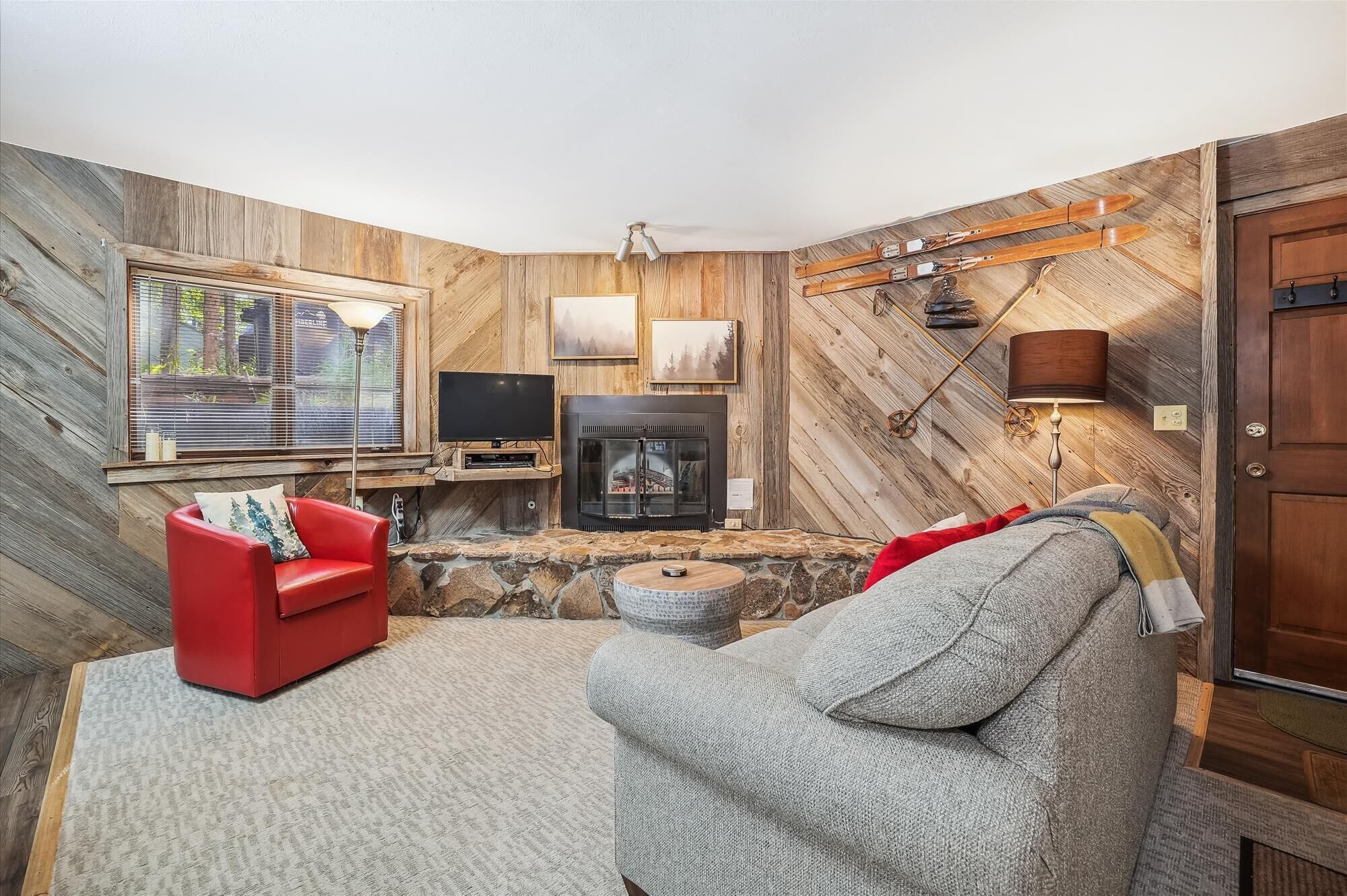 Una sala de estar acogedora con chimenea de piedra, un sofá rojo y un sillón gris.