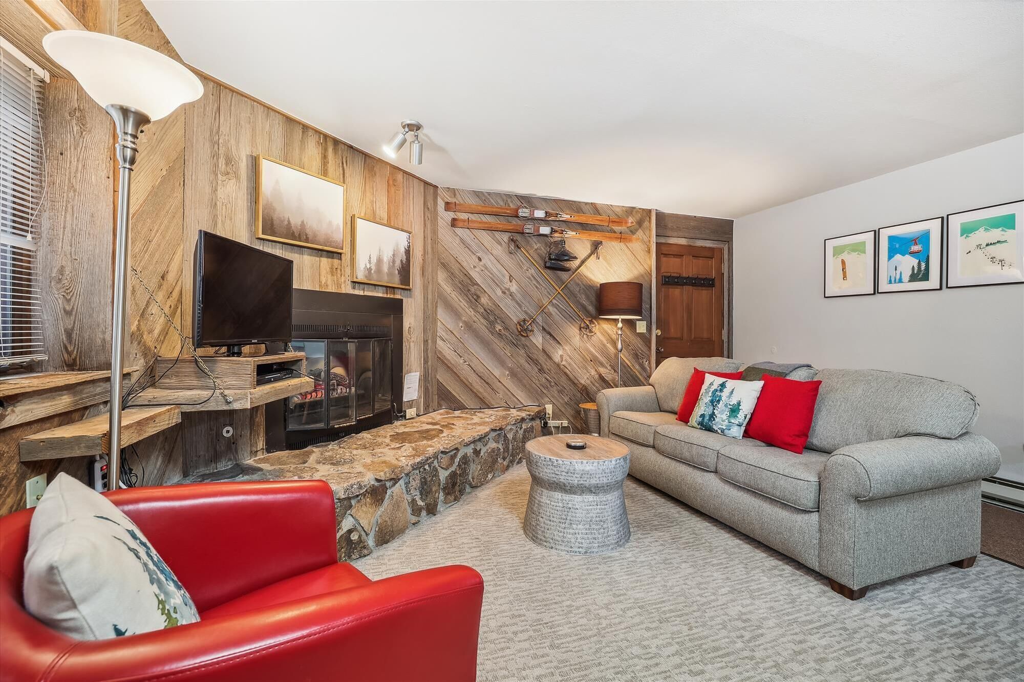 A cozy living room with a fireplace, a red leather sofa, a grey sofa, and a stone coffee table.