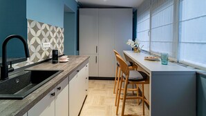 A modern kitchen with a black sink, white cabinets, and a patterned backsplash. There are two wooden chairs and a small table with a glass container. - Celestial Azure Tranquil 1BR Piata Universitatii (Bucharest)