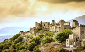 An ancient stone castle with ruins on a hillside, surrounded by greenery and overlooking a body of water. - Platsa Seaview Retreat - A Stone-built Escape (West Mani)