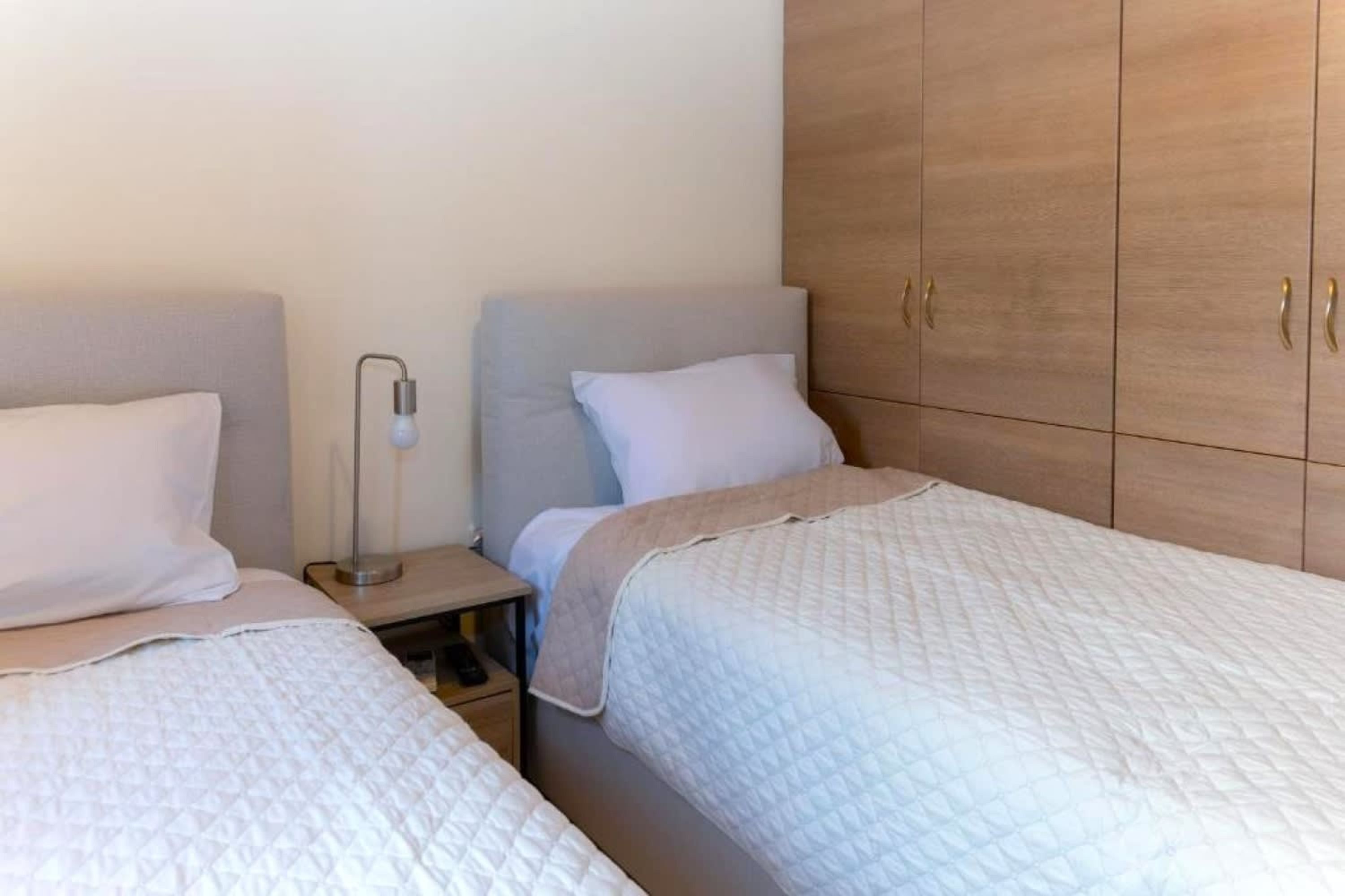 Een slaapkamer met twee bedden, een nachtkastje met een lamp en houten kledingkasten.