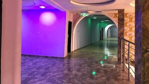 Un couloir moderne avec un mur illuminé de lumière violette, un sol en marbre et un motif géométrique sur le mur.