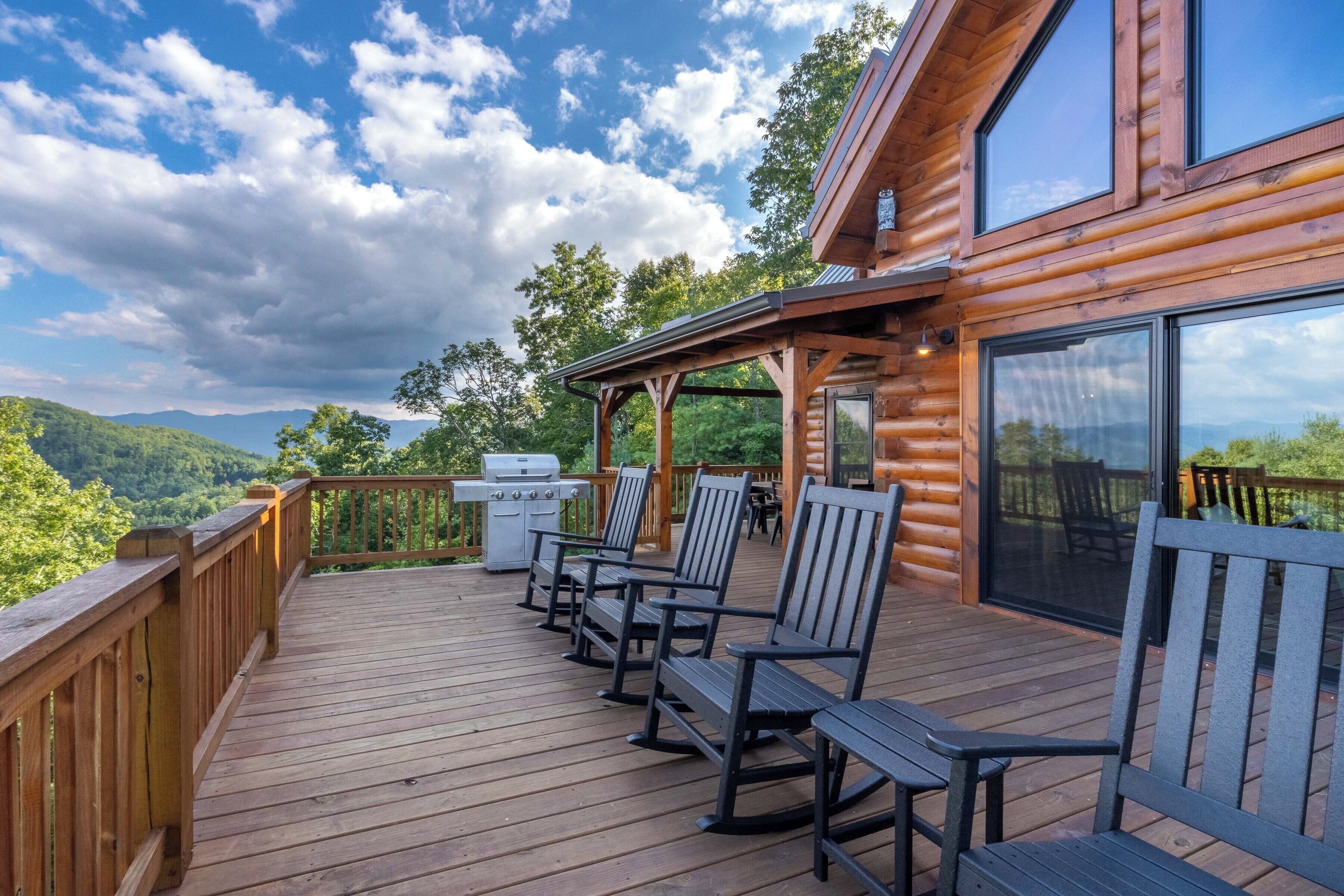A wooden deck with outdoor seating and a grill, overlooking a mountainous landscape.