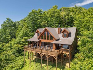 Une cabane en rondins dotée d’une terrasse et de nombreuses fenêtres, entourée d’une forêt dense.