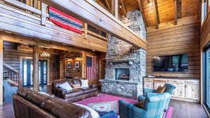 A spacious living area with a stone fireplace, leather sofas, and a large TV. - High Country Cabin -  Mountain & Fontana Lake Views - Hot Tub (Almond)