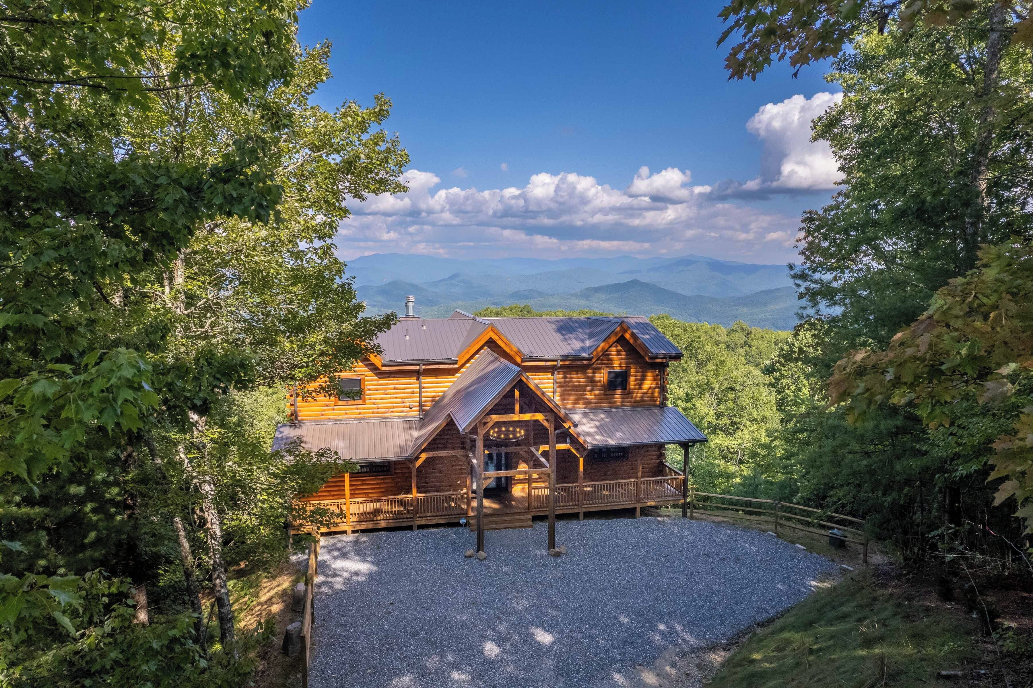 Une cabane en bois dotée d’un porche et d’une allée en gravier, entourée d’arbres et avec des montagnes en arrière-plan.