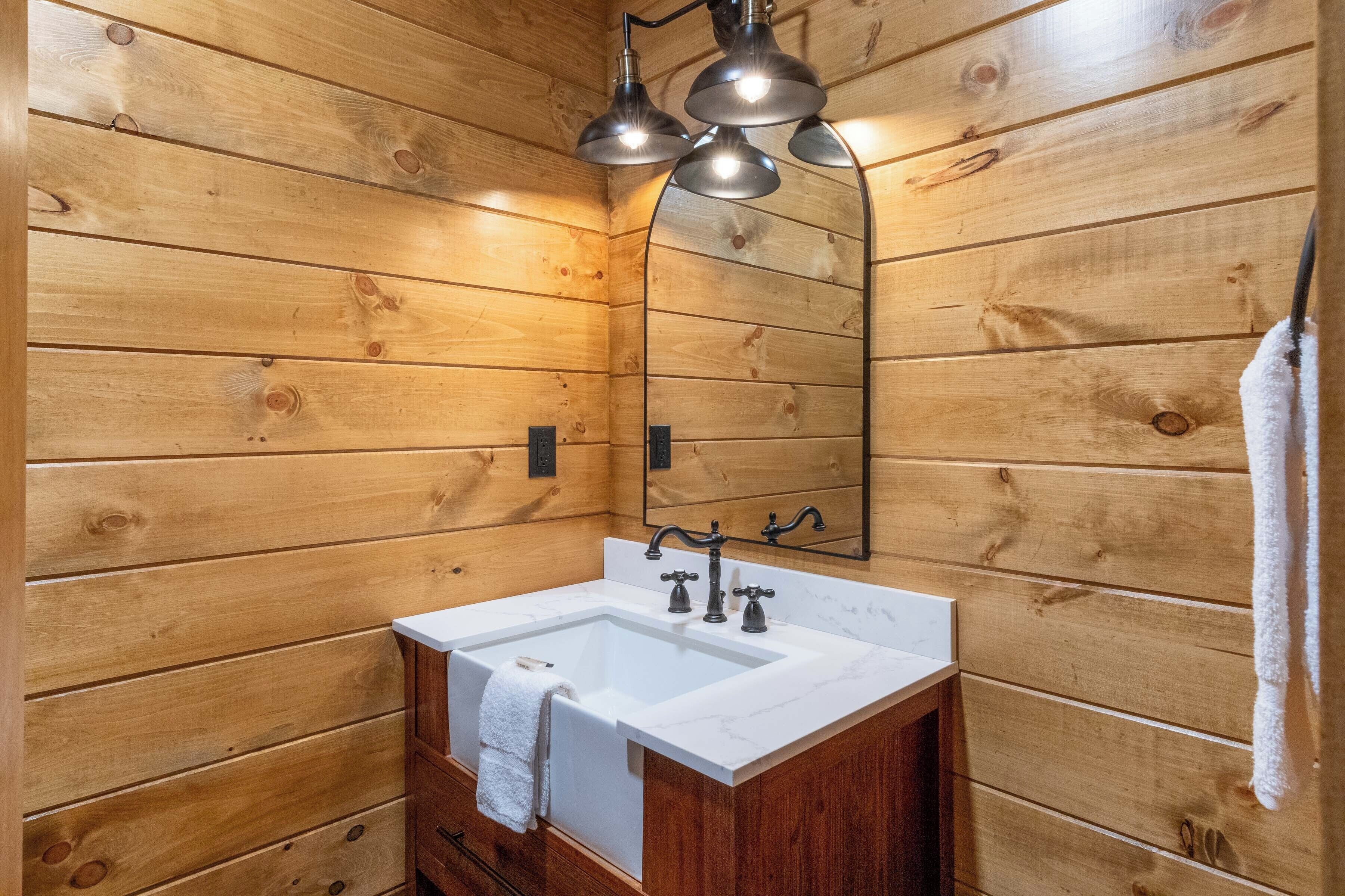 A wooden cabin bathroom with a white sink, two faucets, and a mirror above the sink.