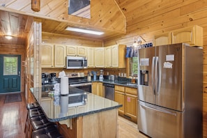A kitchen with wooden cabinets, a stainless steel refrigerator, a microwave, and a granite countertop. - Cabin w Mtn View/Pool Table|Air Hockey|Arcade|Hot Tub (Sevierville)