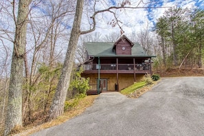 Un chalet à deux étages doté d’un balcon, entouré d’arbres.