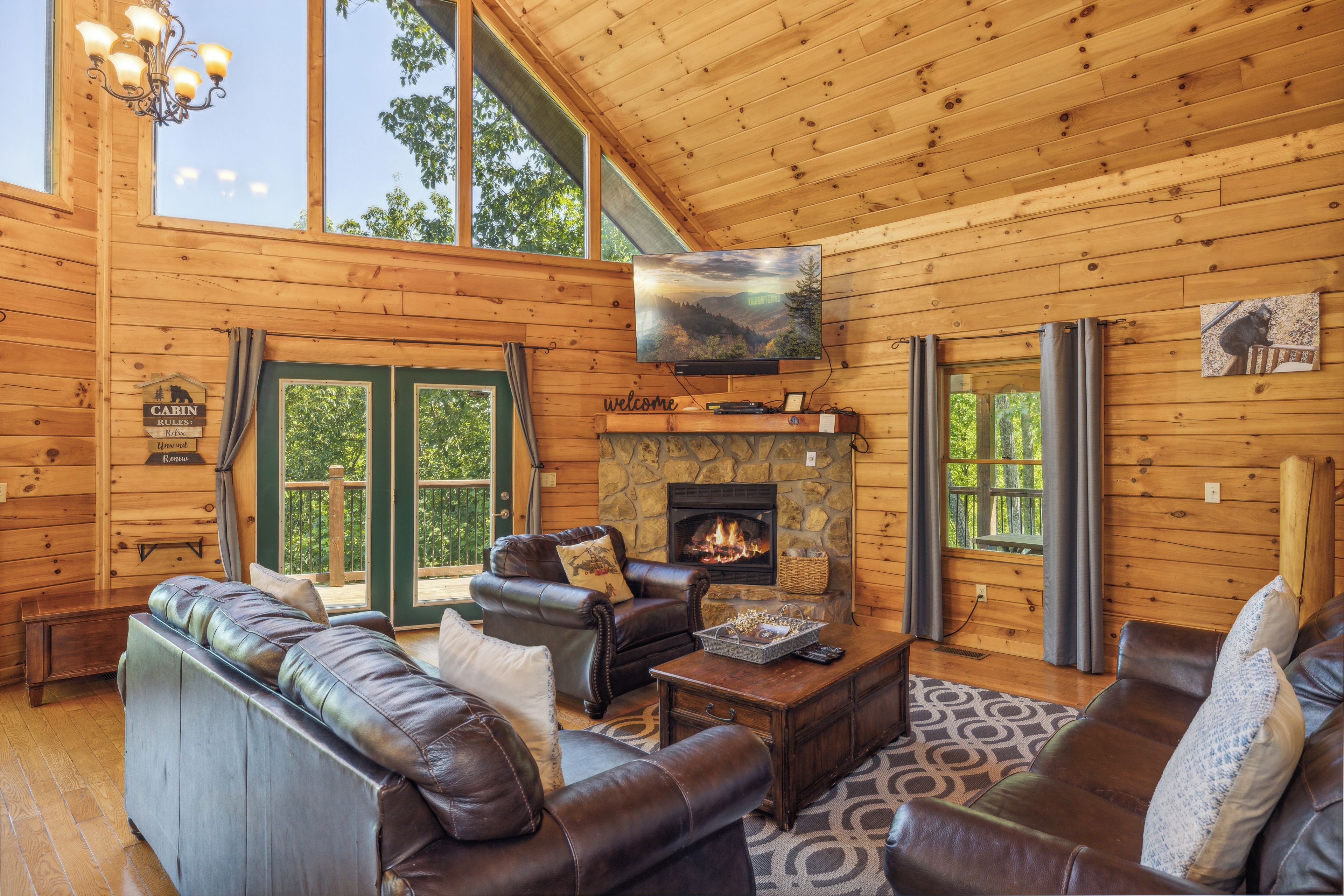 A cabin interior with a fireplace, leather sofas, a TV, and large windows.