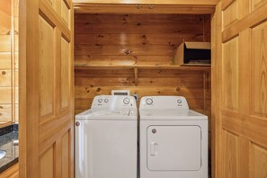 A laundry room with two white front-loading washers and dryers, wooden walls, and a countertop with a sink. - Cabin w Mtn View/Pool Table|Air Hockey|Arcade|Hot Tub (Sevierville)