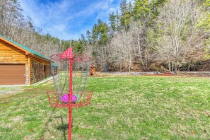 A wooden cabin with a green roof, a red basketball hoop, and a playground area with a slide and swings. - Cabin w Mtn View/Pool Table|Air Hockey|Arcade|Hot Tub (Sevierville)