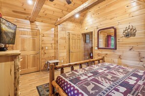 A wooden cabin interior with a bed, wooden walls, a mirror, and a framed picture. - Cabin w Mtn View/Pool Table|Air Hockey|Arcade|Hot Tub (Sevierville)