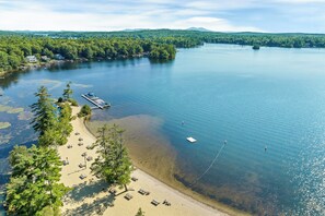 An aerial view of a lakeside property with a dock, beach, and surrounding forest.