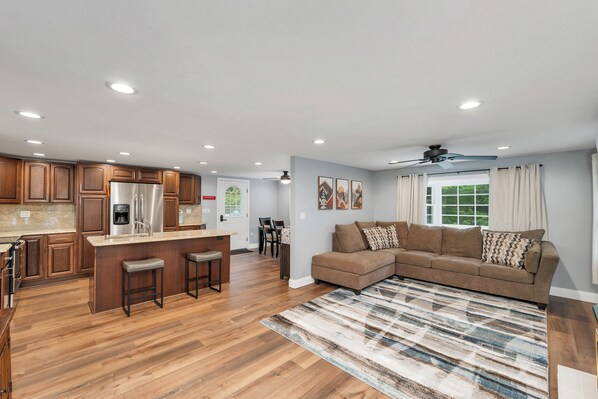 A modern kitchen with wooden cabinets, a stainless steel refrigerator, and a bar area with stools.