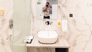 A bathroom with a marble wall, a glass shower enclosure, a sink, and a mirror. - Hotel Miracle Resorts (Phagwara)