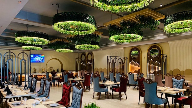 A spacious dining area with multiple tables and chairs, decorative ceiling plants, and a television screen. - Hotel Miracle Resorts (Phagwara)