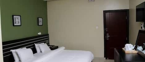 Una habitación de hotel con cama, escritorio, silla, televisor y puerta.