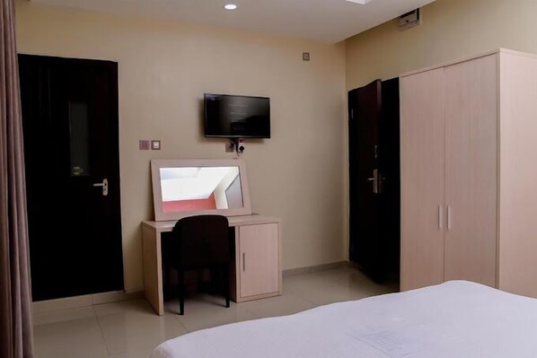 A hotel room with a bed, a desk with a computer, a television, and a wardrobe.