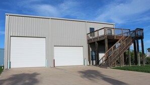 A large industrial building with two large garage doors, a wooden staircase leading to a balcony, and a clear sky. - 308 Copano - Vast open design, modern & can accommodate big groups (Port Mansfield)