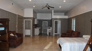 A spacious room with a large bed, a brown leather sofa, a wooden chair, and a desk area. - 308 Copano - Vast open design, modern & can accommodate big groups (Port Mansfield)