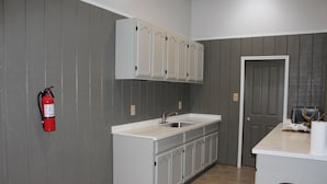 A kitchen with a white countertop, a sink, and cabinets. There is a fire extinguisher mounted on the wall. - 308 Copano - Vast open design, modern & can accommodate big groups (Port Mansfield)