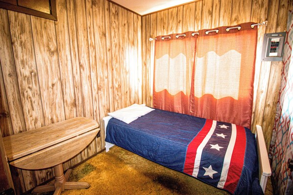 Una cama individual con una colcha azul y roja, un banco de madera y una pared de madera.
