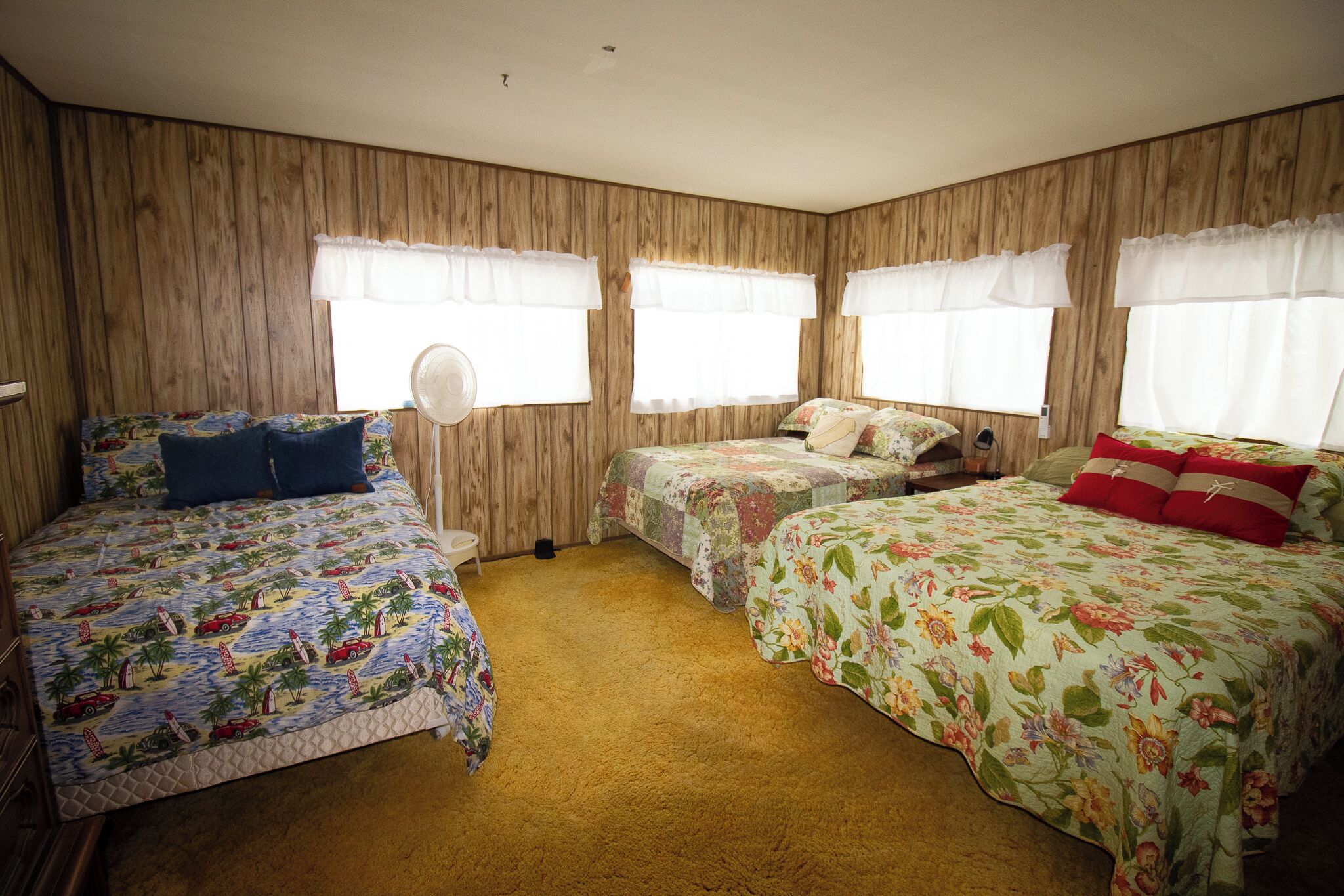 Een kamer met drie bedden, elk voorzien van bloemenbedrukkingen, houten paneelwanden en witte gordijnen.