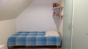 A small, single-bed room with a sloped ceiling, a white door, and a shelf with books and a toy. - Erdeven, Small holiday home (Erdeven)