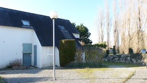 A house with a sloped roof, a gravel driveway, and a hedge in front.