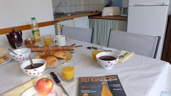 A breakfast table with croissants, coffee, juice, and a magazine.