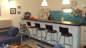 A compact kitchen with a bar area, bar stools, a refrigerator, and a clock on the wall.