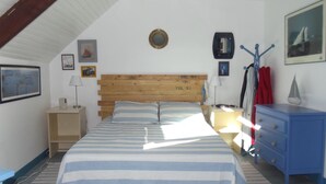 A bedroom with a wooden headboard, a bed with striped bedding, a nightstand, a dresser, and a mirror on the wall.