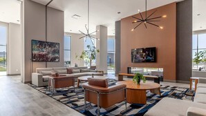 Un vaste espace de vie comprenant un grand canapé, une table basse et des fauteuils, un téléviseur à écran plat fixé au mur, ainsi qu’une grande fenêtre offrant une vue sur l’extérieur.