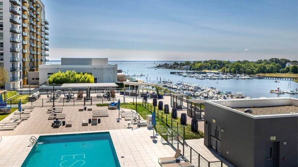 Un espace piscine aménagé sur le toit, avec des chaises longues, une piscine et une vue sur un port de plaisance rempli de bateaux.