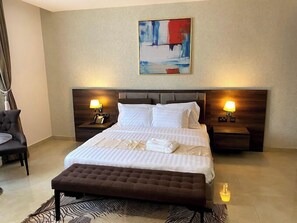 Habitación de hotel con una cama grande, dos mesitas de noche con lámparas, una silla y un felpudo con estampado de cebra.