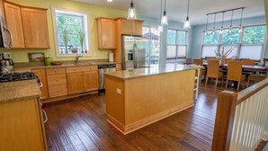 A modern kitchen with wooden cabinets, a central island, stainless steel appliances, and a dining area with wicker chairs. - Hillside retreat in Beachwalk Resort for 10 (Michigan City)