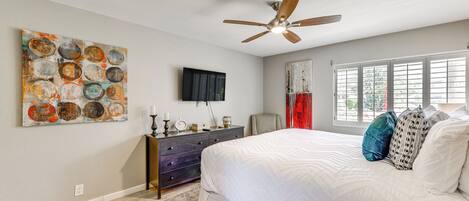 A bedroom with a bed, a ceiling fan, a dresser, a TV, and a window with curtains.