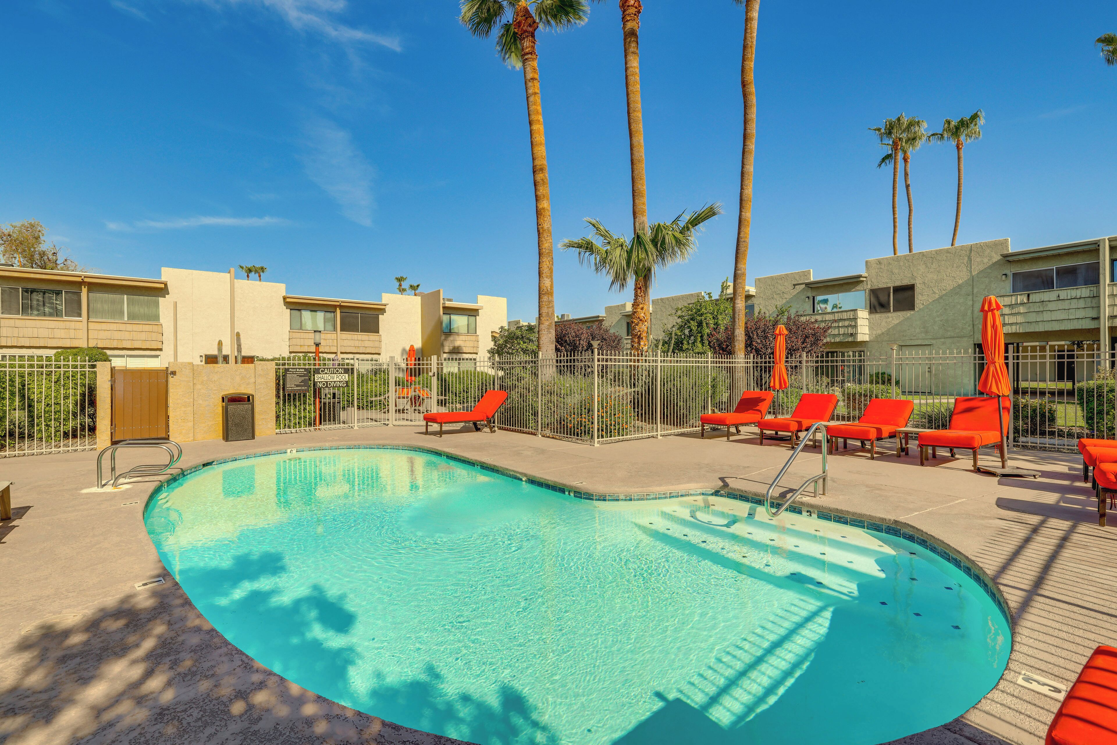 A swimming pool with red lounge chairs and palm trees.