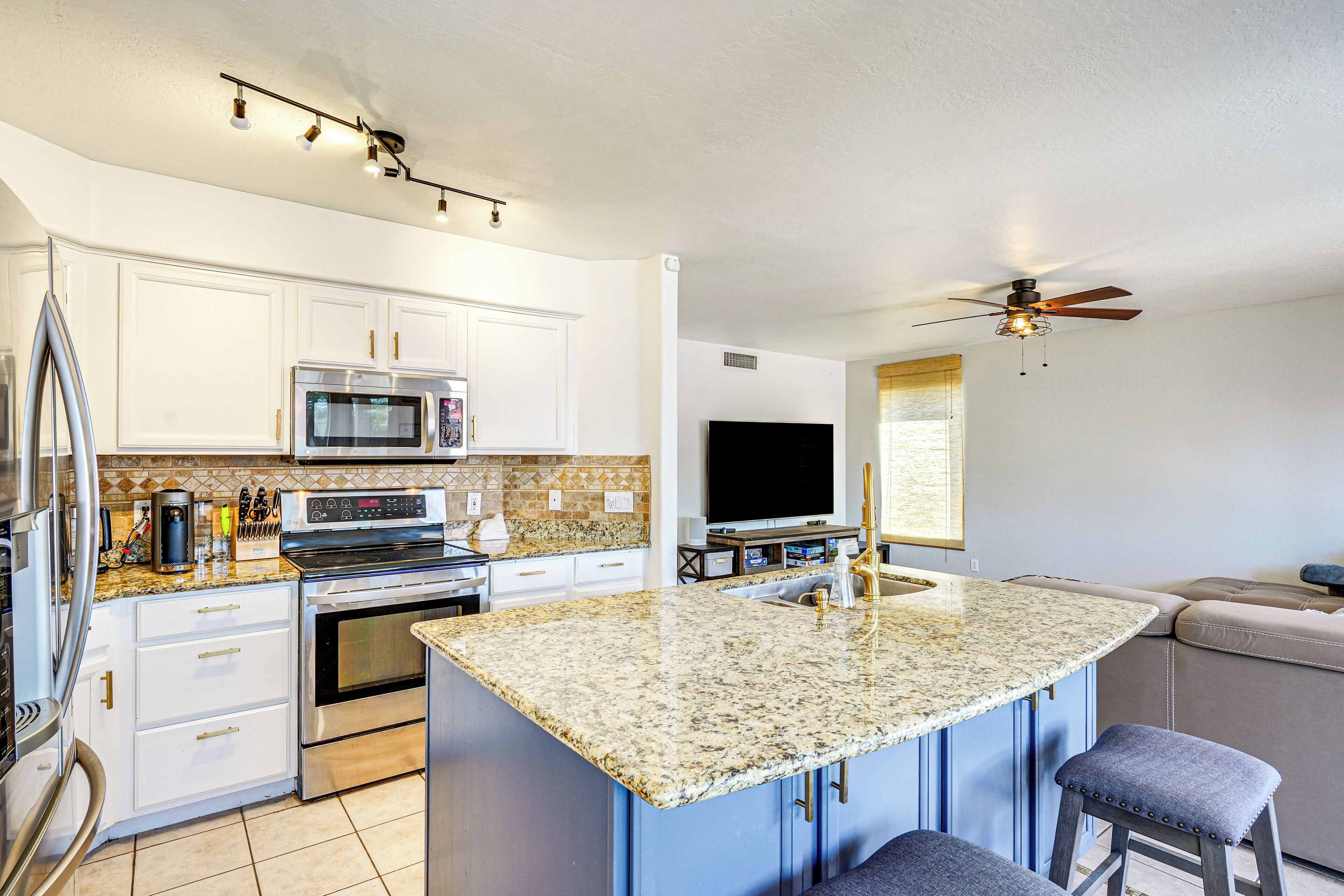 A modern kitchen with white cabinets, a granite countertop, stainless steel appliances, and a built-in TV.
