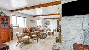 A spacious living room with a fireplace, wooden furniture, and a large window. - Family Beach Days: Dog-friendly Cape Cod Condo (Dennis Port)