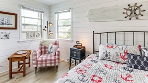 A bedroom with a bed, a chair, a small table, and a nightstand. - Family Beach Days: Dog-friendly Cape Cod Condo (Dennis Port)