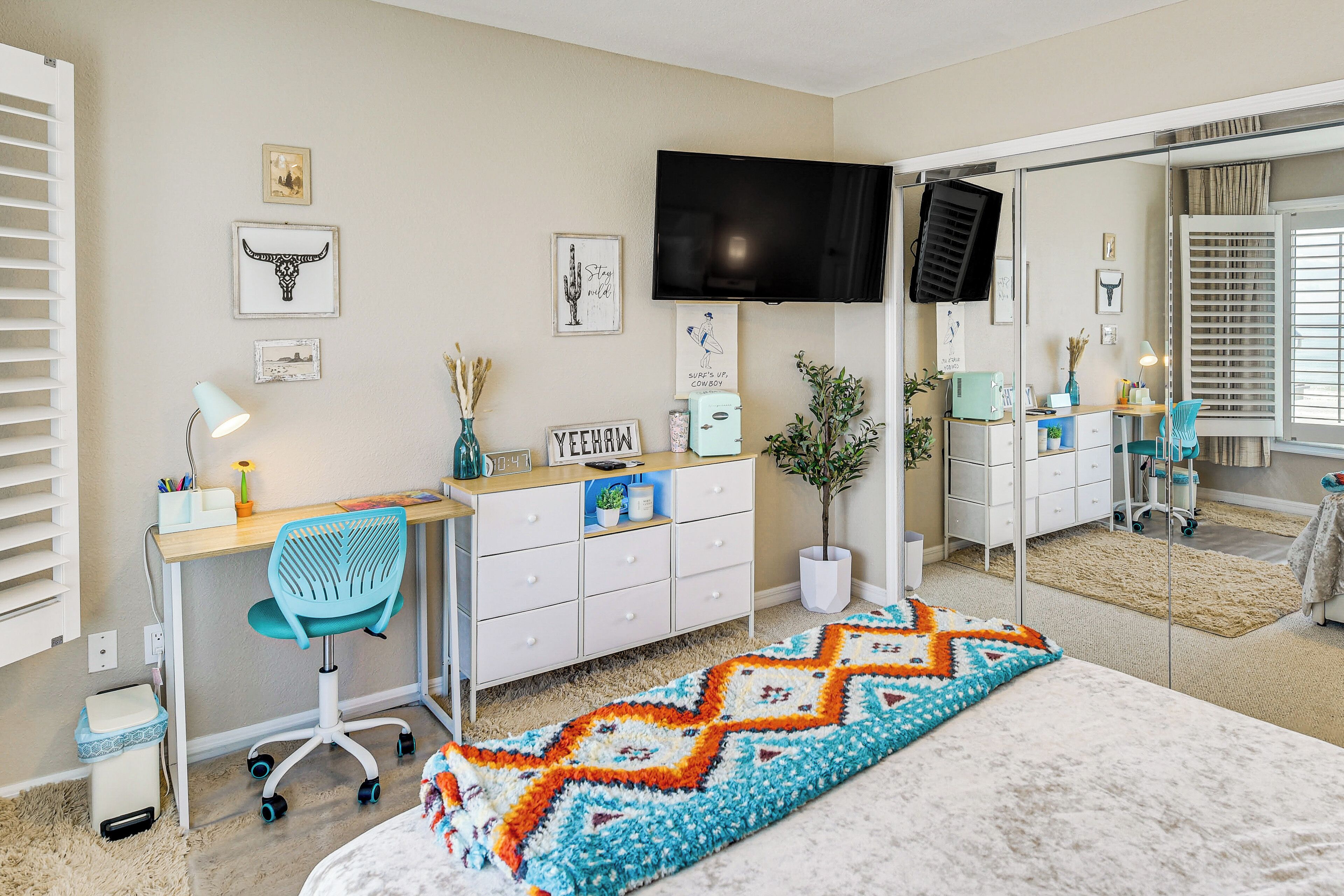 A bedroom with a bed, a desk with a chair, a TV, and a mirror.
