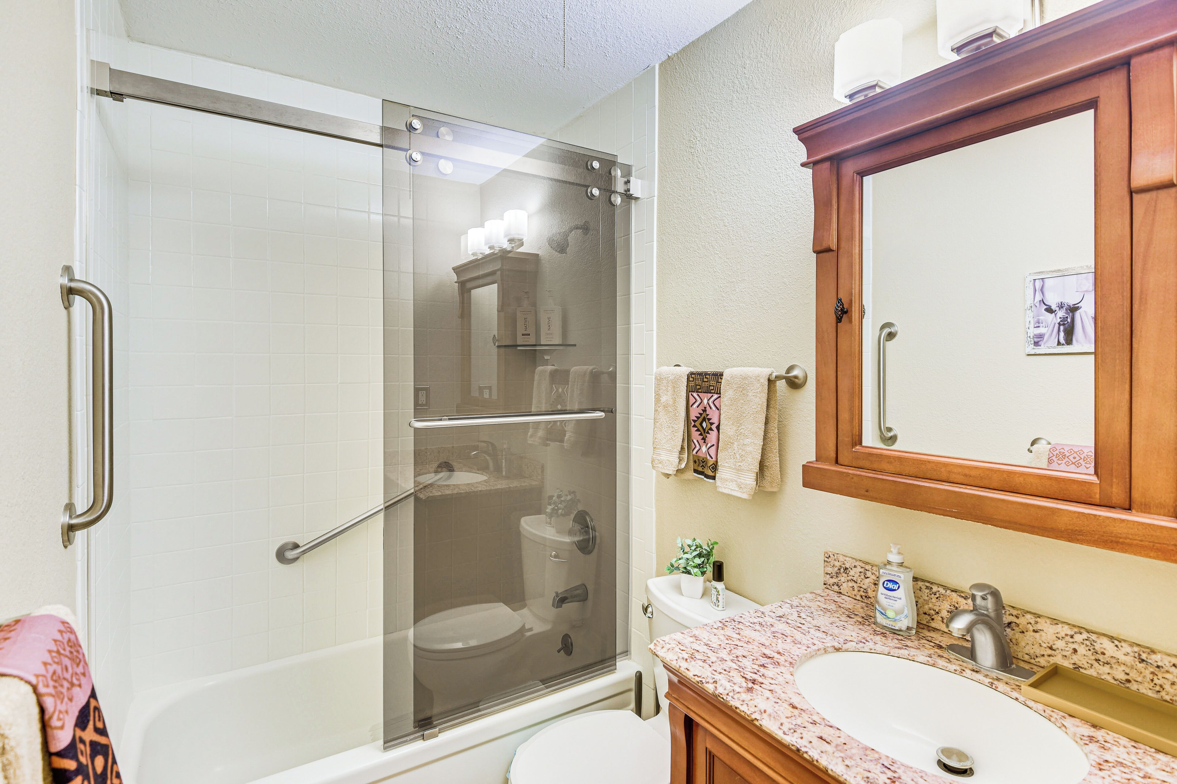 Un baño con ducha envuelta en vidrio, un lavabo blanco y un mueble de tocador de madera.